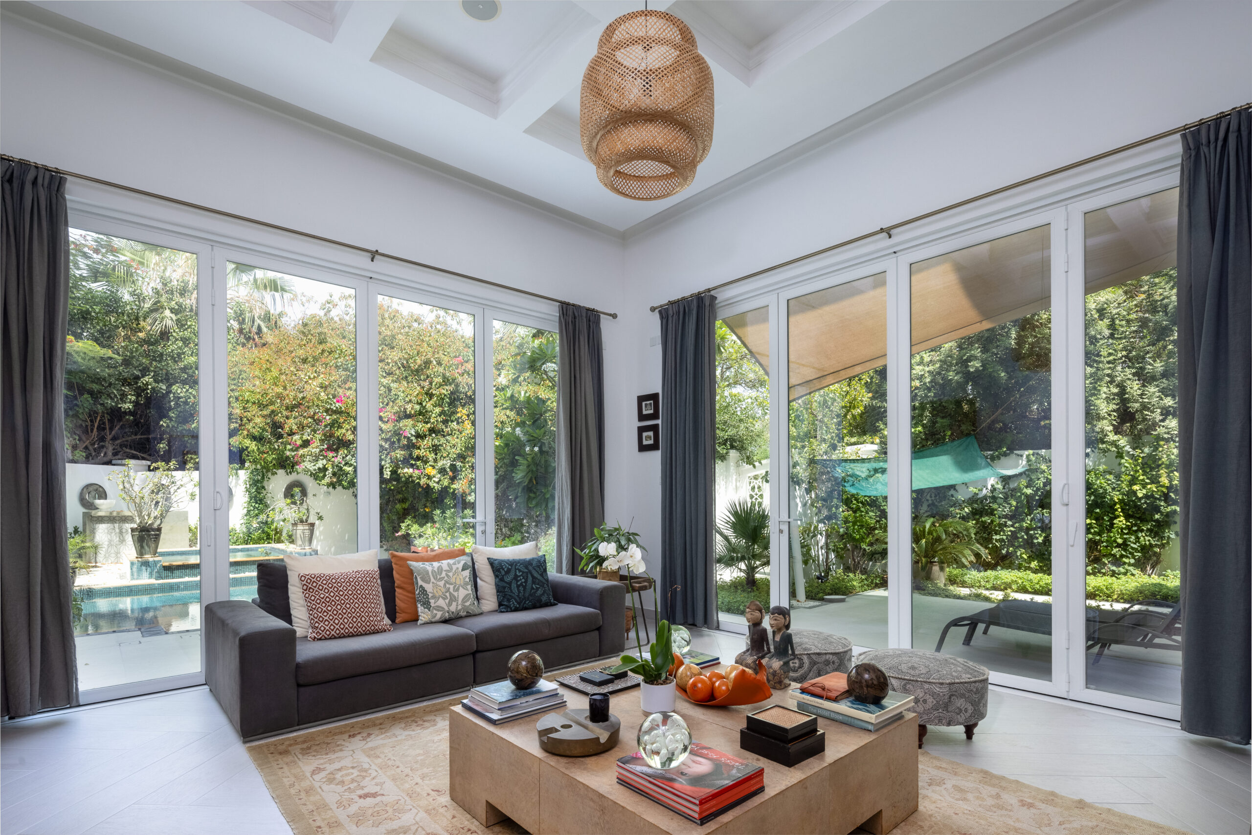 Bright villa living room with large white-framed sliding doors opening onto a garden and pool
